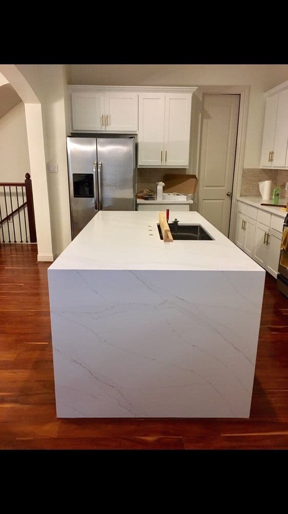 White quartz waterfall island with white cabinets and hardwood floors
